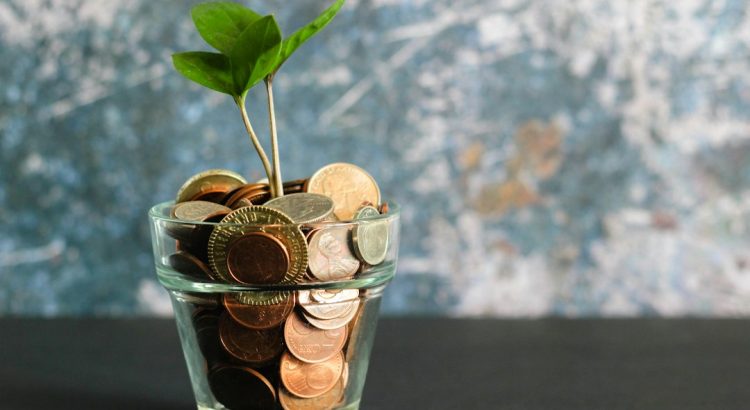 A glass pot filled with coins and a small plant growing from the top, symbolizing growth and investment.
